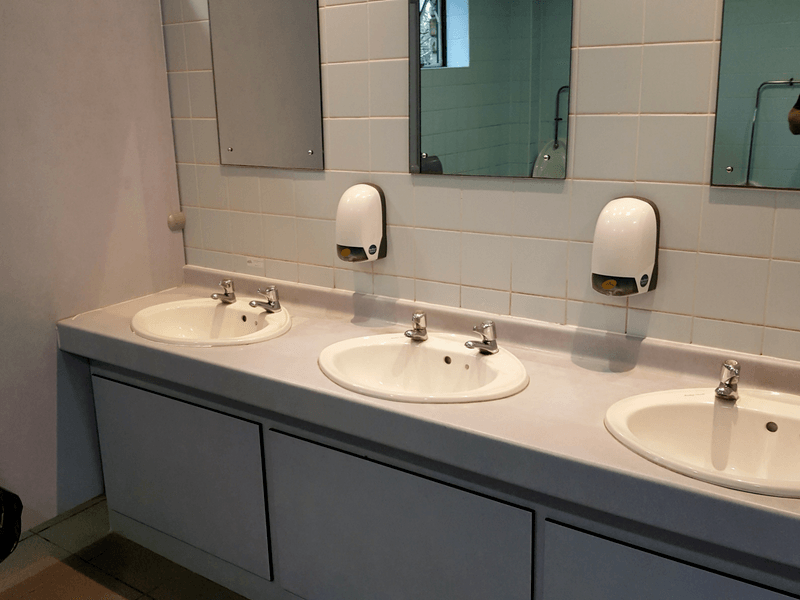 Three sinks and two soap dispensers in a bathroom.