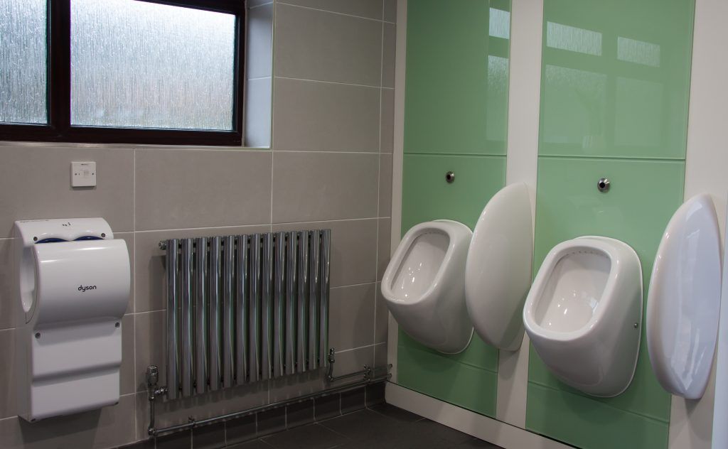 Two urinals, radiator and hand dryer inside a washroom.