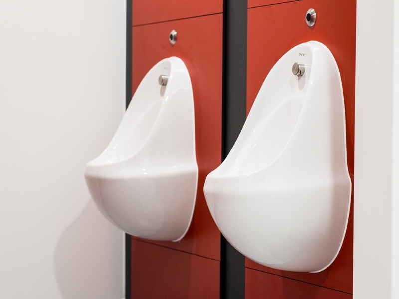 Two urinals on a red wall.
