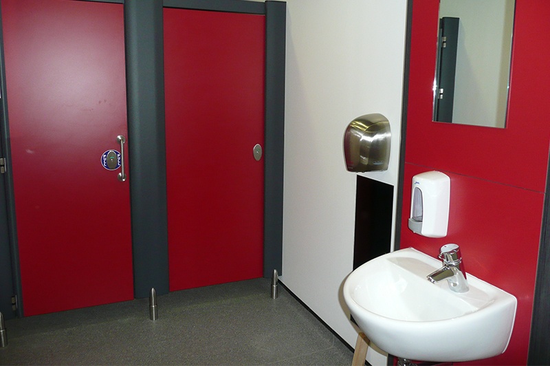 Red washroom with two toilet cubicles and a sink.