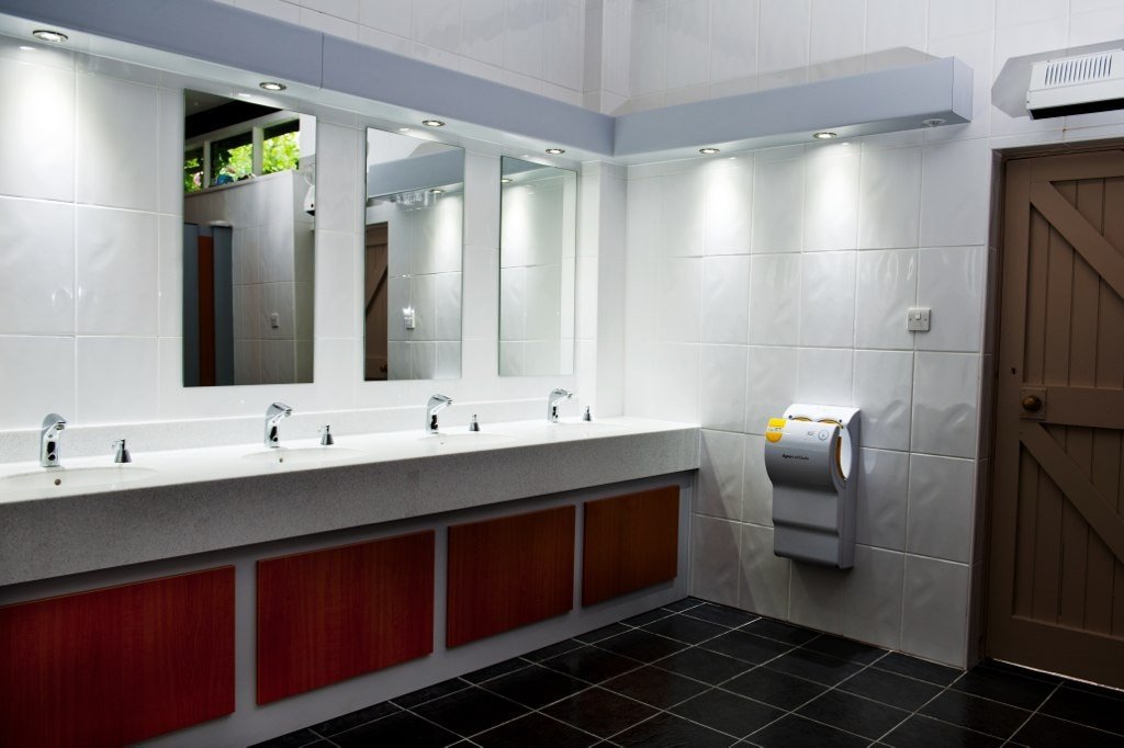 Interior of a washroom with four sinks and a hand dryer.