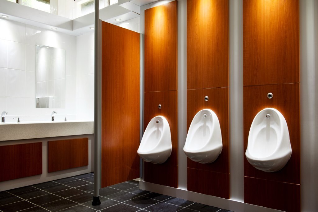 Inside of a washroom with three urinals and two sinks in the background.