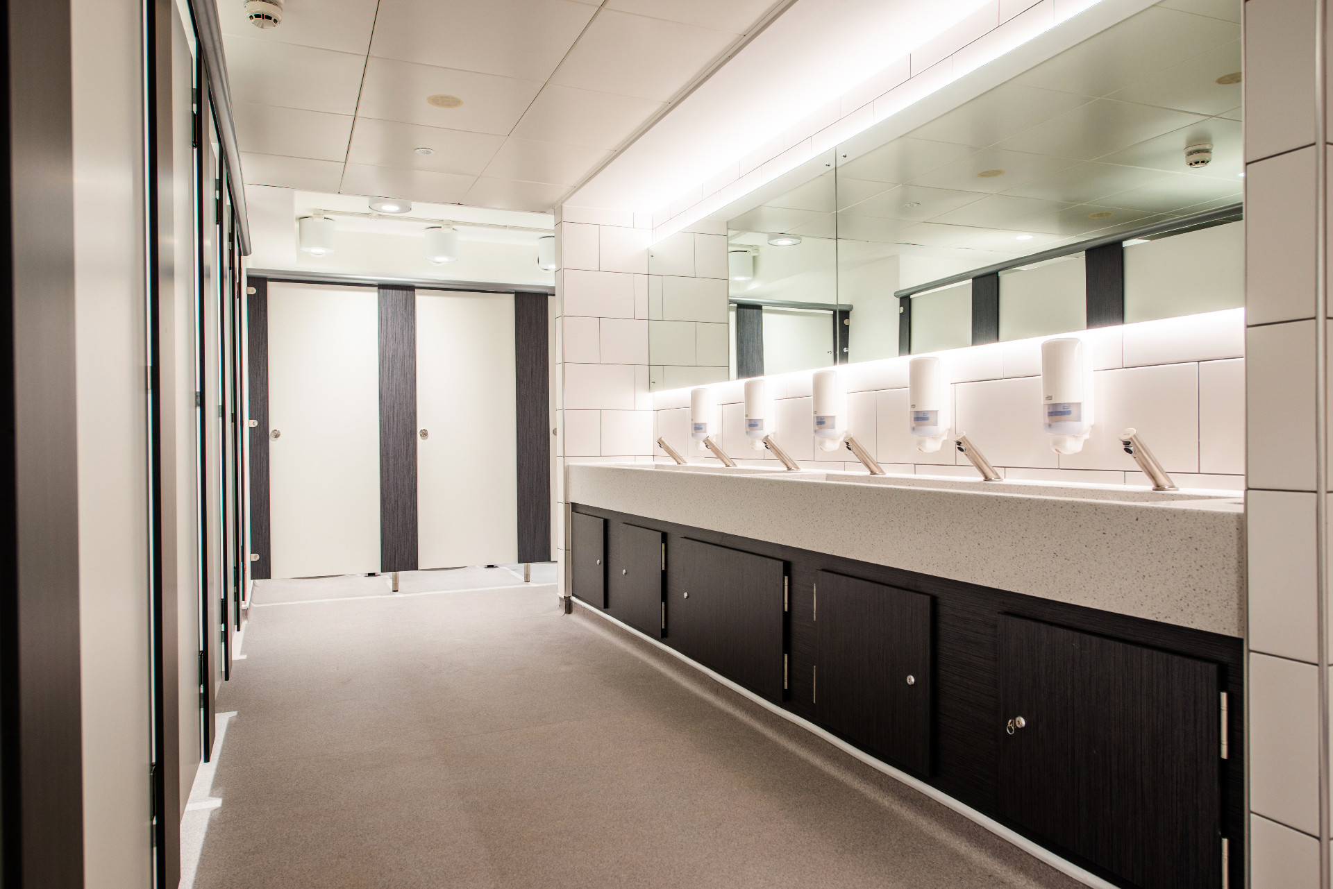 Row of basin and toilet cubicles with lighting and mirrors.
